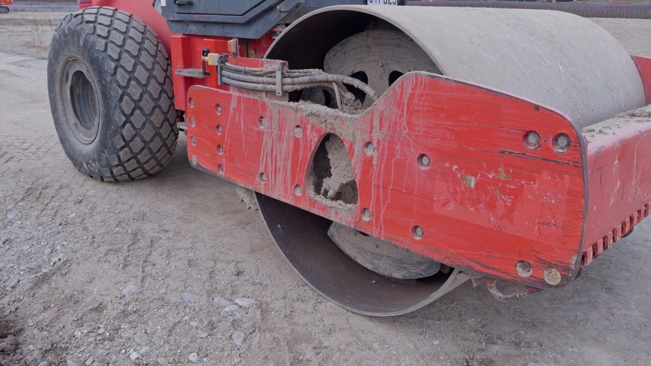 Closeup of road roller compacting dirt at a construction site with open terrain