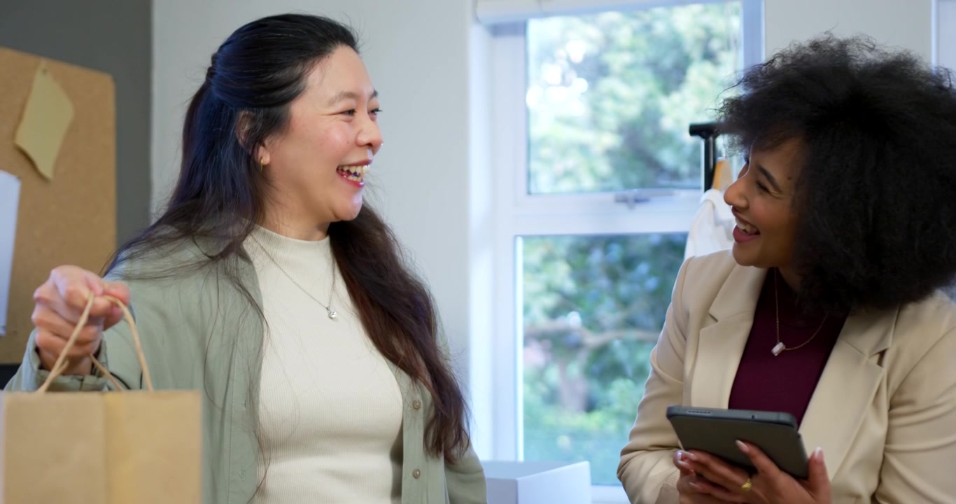 Diverse female colleagues presenting brown paper bag, consulting tablet at shop confirming order