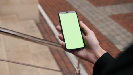 close-up view of a person holding a smartphone swiping pages on mockup green screen outdoor