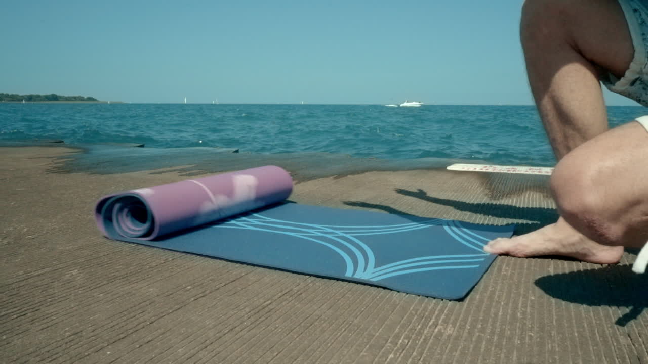 un tipo extendiendo una alfombra de yoga por el mar. un joven preparándose para la meditación por el mar.