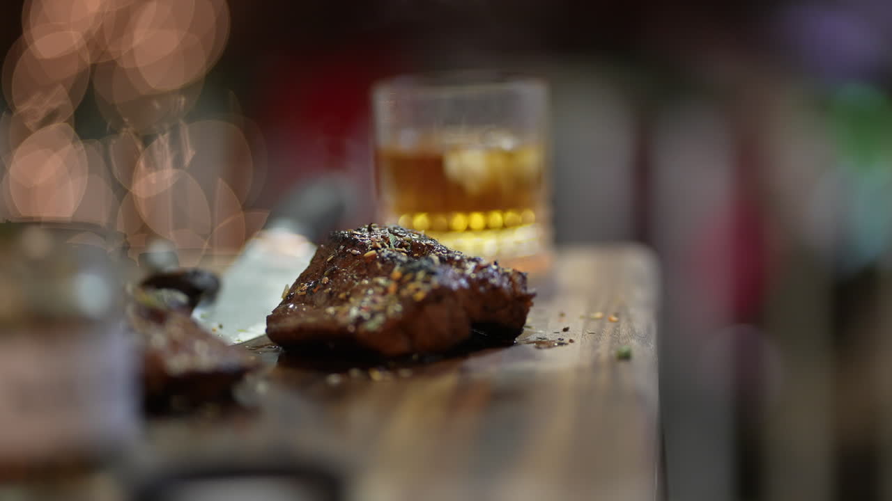 Spostamento della messa a fuoco da una bistecca in crosta di erbe a un bicchiere di bourbon.