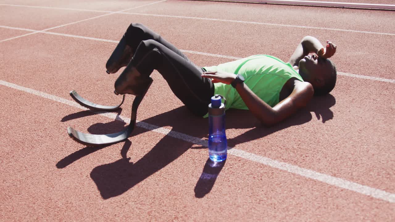 Uomo di etnia mista disabile con gambe protesiche sdraiato sulla pista di atletica.