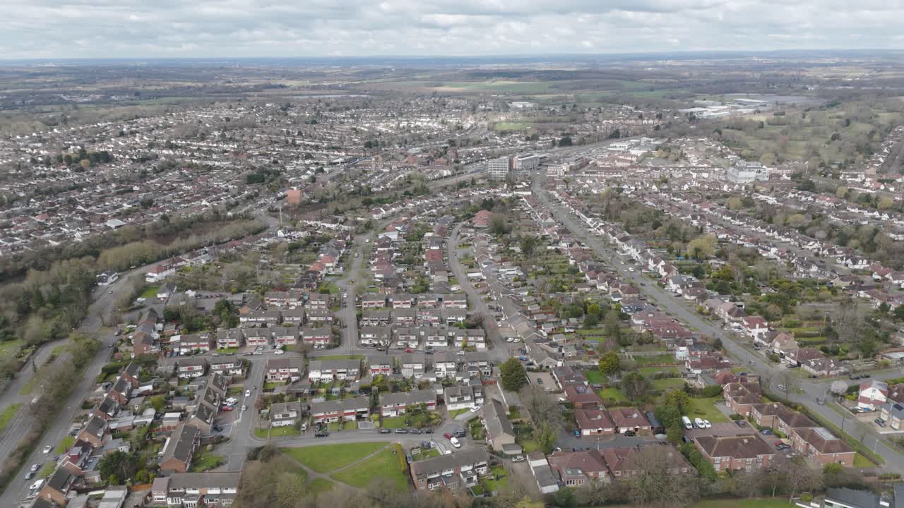 Aerial overview of orderly commuter suburb with tree-lined avenues, red-roof semi-detached houses, tennis courts and school playing fields forming a leafy residential grid