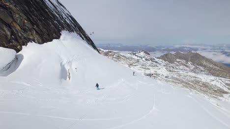 Aerial-tracking-shot-of-snowboarder-speeding-downhill-snowy-mountains-in-sunlight---Austria,Europe