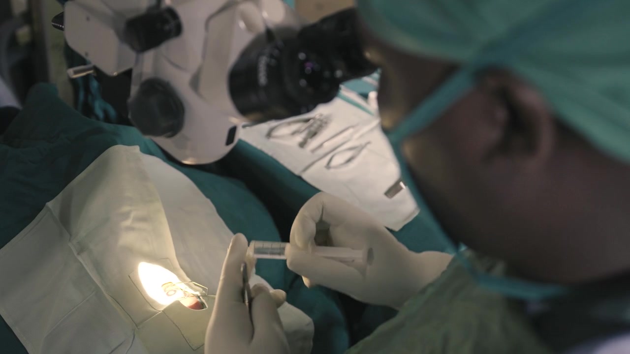 close up of doctor using tweezers in eye and after taking a syringe to insert fluids into the eye during surgery in Africa