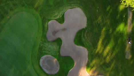 drone shot over golf course showing bunkers, trees, and players during a sunny day and golf practice