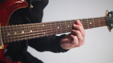 detaillierte nahaufnahme der finger eines gitarristen auf einem roten gitarrenfaden vor einem scharfen weißen hintergrund