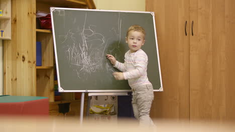 little boy drawing on a chalkboard at kindergarten