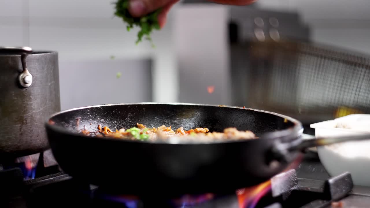 Close up view of a Chef adding herbals and parsley to a beef stew in a frying pan skillet in a restaurant kitchen cuisine in slow motion.