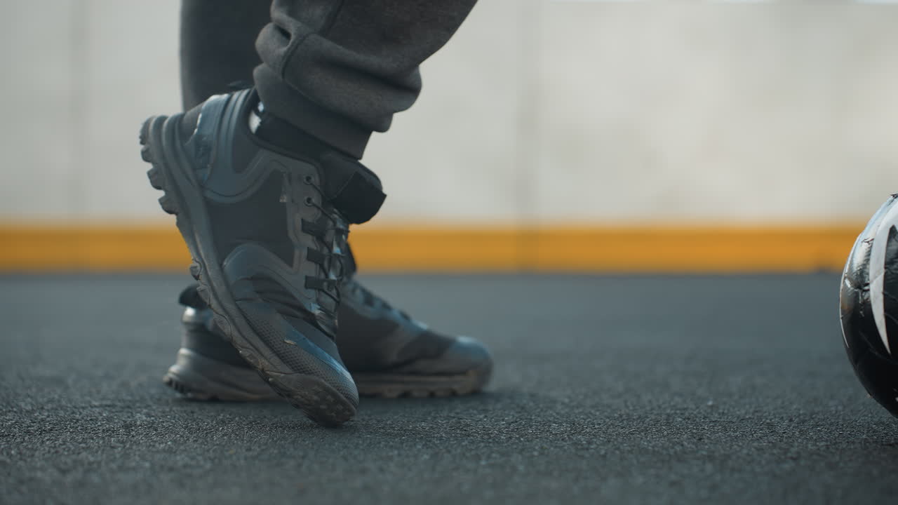 vista de cerca de la pierna lateral de un deportista que demuestra giros controlados del tobillo usando la pierna izquierda y derecha para manipular la pelota de fútbol en la arena deportiva con un fondo con una pared pintada de amarillo