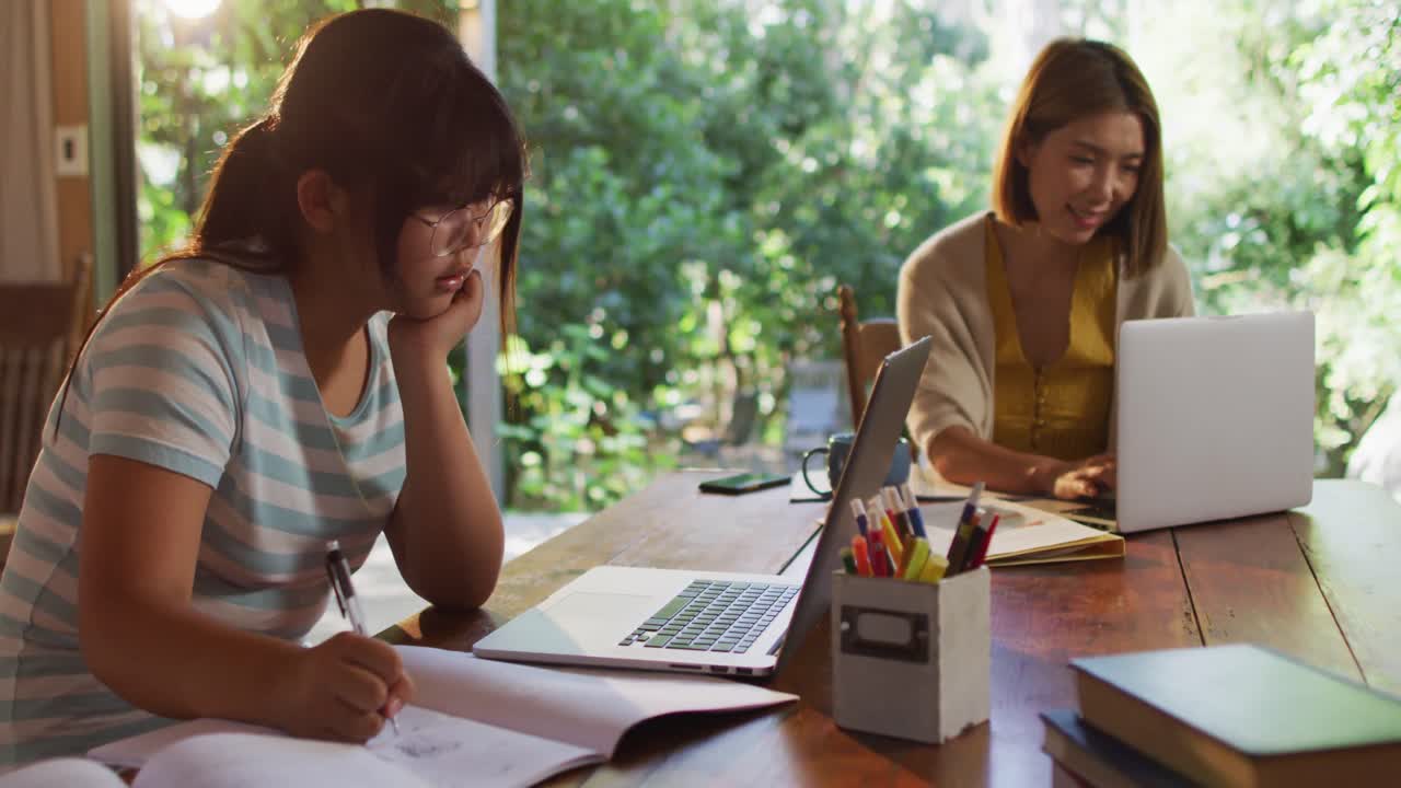 아시아인 어머니와 딸이 노트북을 사용하여 배우고 일합니다.
