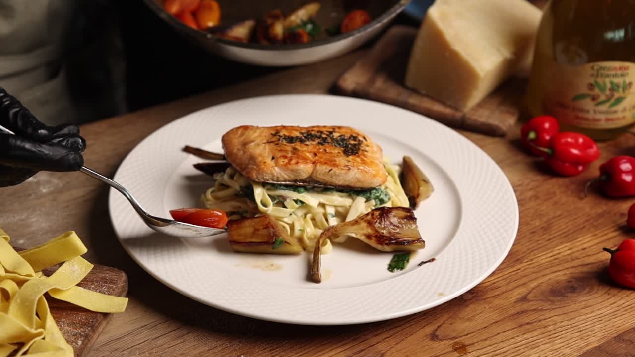 Chef emplatando salmón con pasta tagliatelle y verduras asadas.