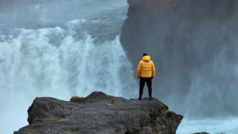 turista masculino de pie en un acantilado junto a la cascada godafoss en islandia - disparo de avión no tripulado