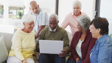 personas mayores felices y diversas hablando y usando computadoras portátiles en el hogar de ancianos