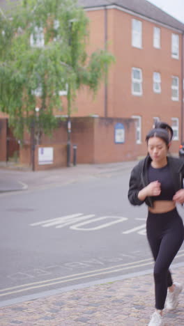 Vertical-Video-Of-Young-Woman-Exercising-Running-Along-Urban-Street-Wearing-Wireless-Earbuds-Shot-In-Real-Time