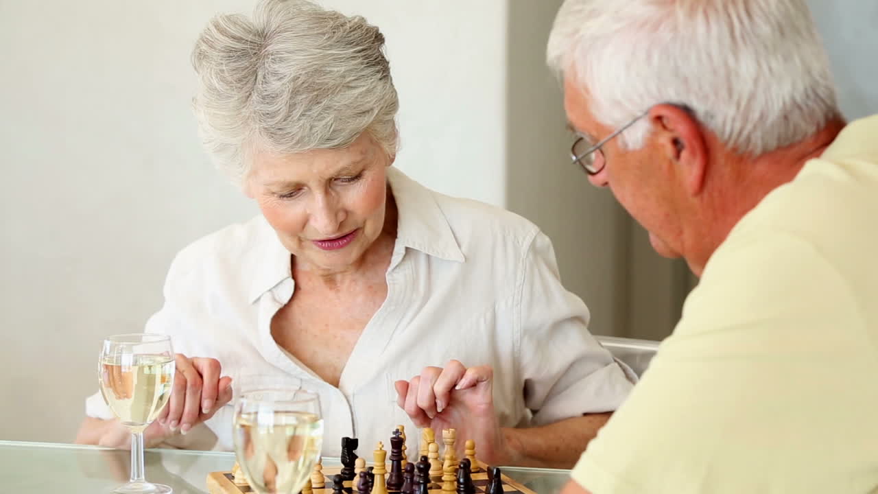 una pareja mayor sentada en la mesa jugando al ajedrez.