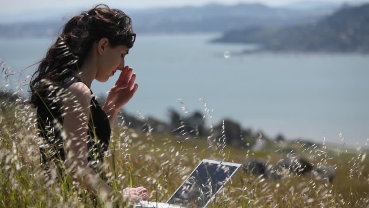 una mujer se sienta en la hierba y usa su computadora portátil