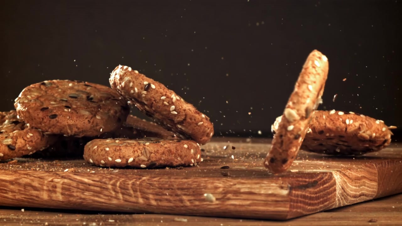 Seeded Oatmeal Cookies Falling in Slow Motion onto a Wooden Board