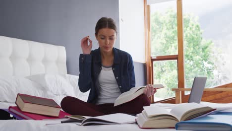 Woman-taking-notes-while-sitting-on-bed-at-home