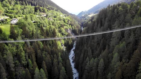 aerial flyover over the goms suspension bridge high up above rhone river valley in valais, switzerland with a hiker standing on the bridge