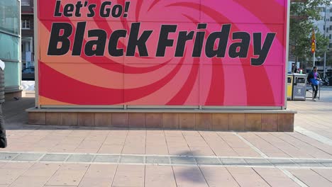 slow-motion footage of pedestrians walking past a banner promoting the upcoming black friday sale and early holiday shopping deals in madrid, spain.