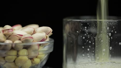 Beer-is-pouring-into-glass-on-black-background.-Bowl-of-pistachios-nuts