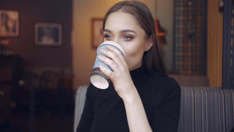 Gentle-young-woman-holding-carefully-cup-of-coffee-and-drinking