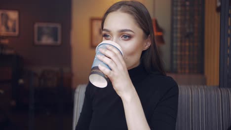 gentle young woman holding carefully cup of coffee and drinking