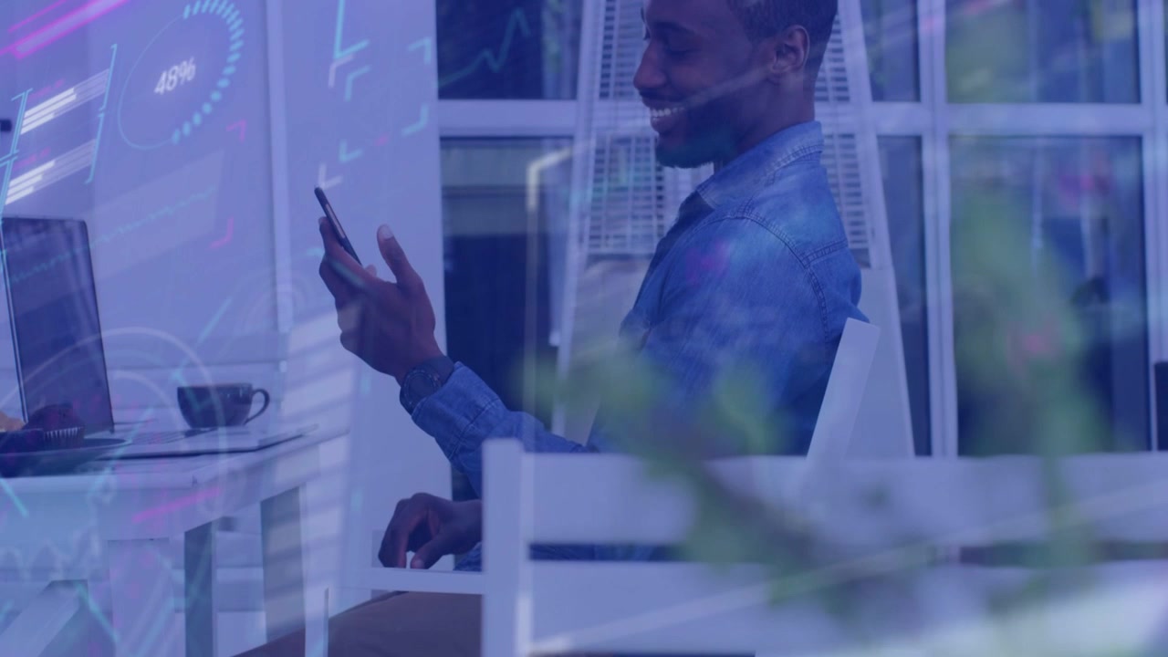 Male employee tapping phone, glancing laptop, data charts appearing over desk showing tech metrics