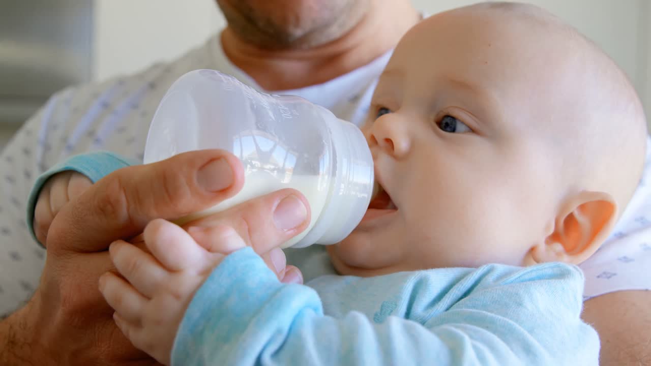 padre alimentando con leche a su bebé en casa 4k