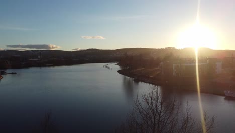 sun glaring through trees during ascending aerial from skien norway - hjellevannet lake in telemark canal facing north towards stromdal area