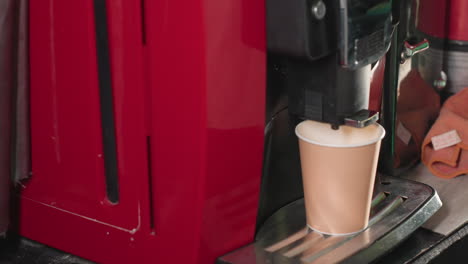 close-up shot of a coffee machine dispensing espresso into a paper cup. the machine's nozzle is visible as it releases foam or milk, emphasizing the beverage preparation process in a caf setting