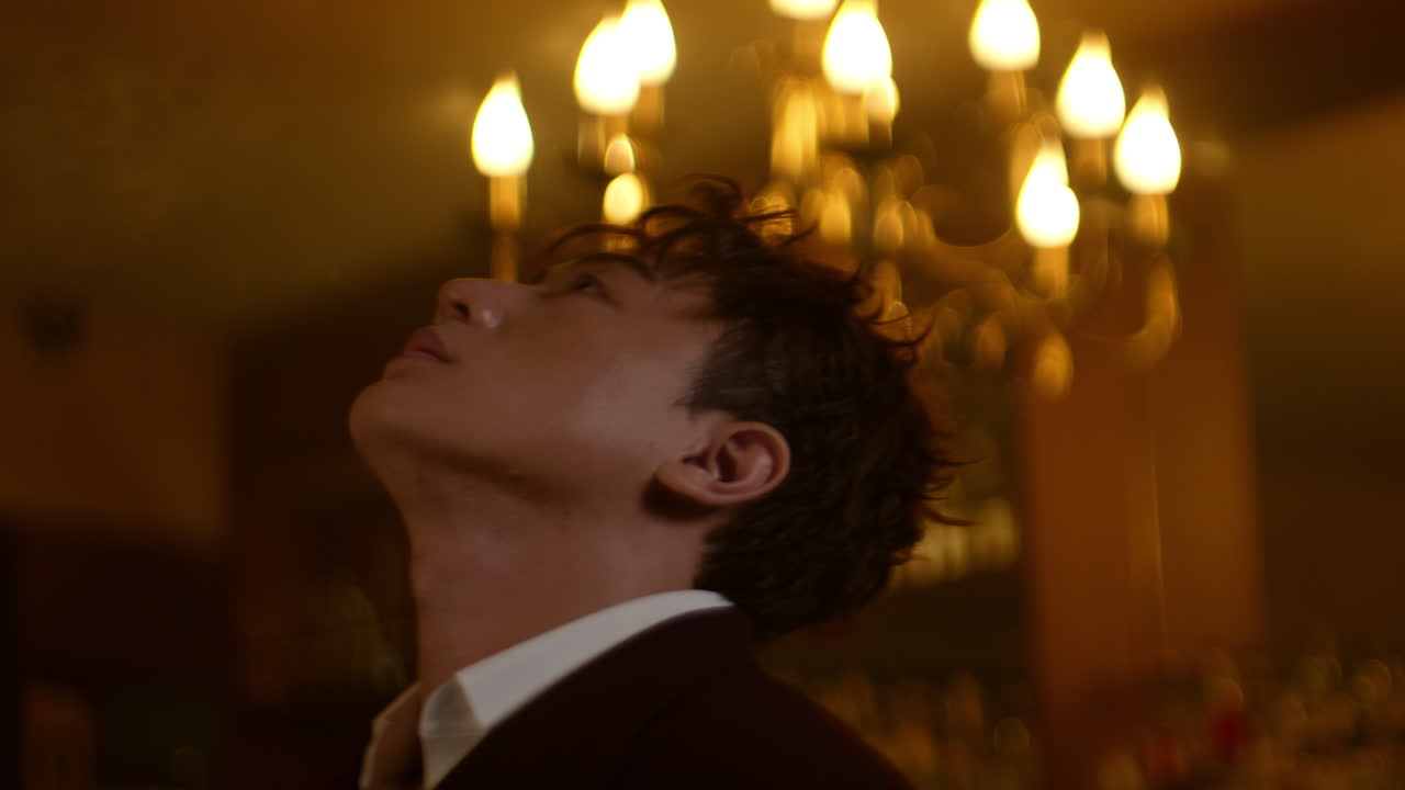 A man gazes upward, lost in thought, surrounded by warm, soft lighting