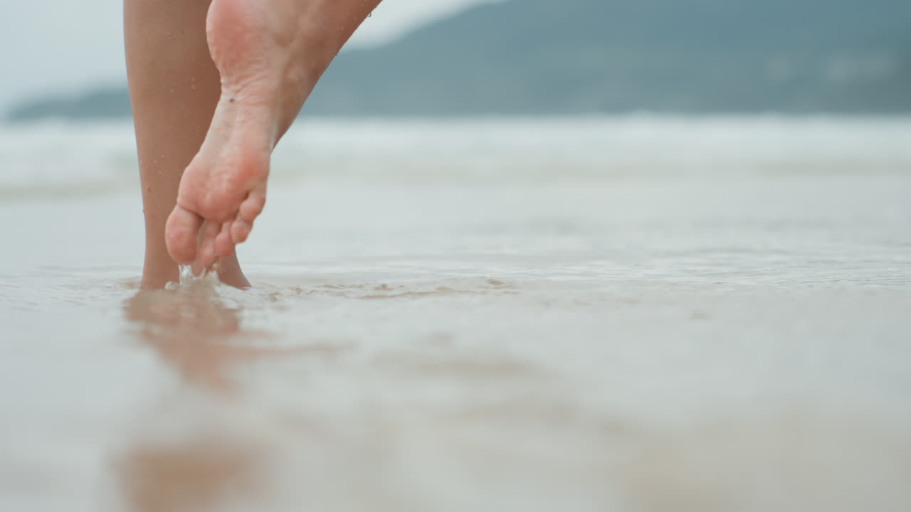 Passi delicati sulla riva dell'isola, passi aggraziati con piccoli schizzi, sabbia morbida e bagnata sotto i piedi, orizzonte lontano cinematografico, viandante romantico, ballerina contemporanea, camminatore consapevole.
