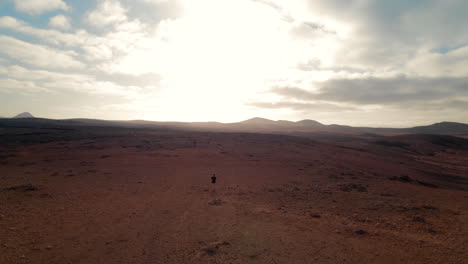 lonely person walking through a rocky desert with sun setting, the terrain is rugged and rocky
