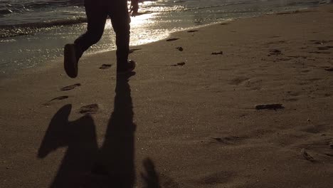 niño silueteado sombra corriendo a cámara lenta a través de la playa de arena dorada de portugal al amanecer