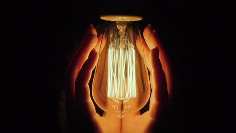 back view of man warms his hands near a light bulb in the dark