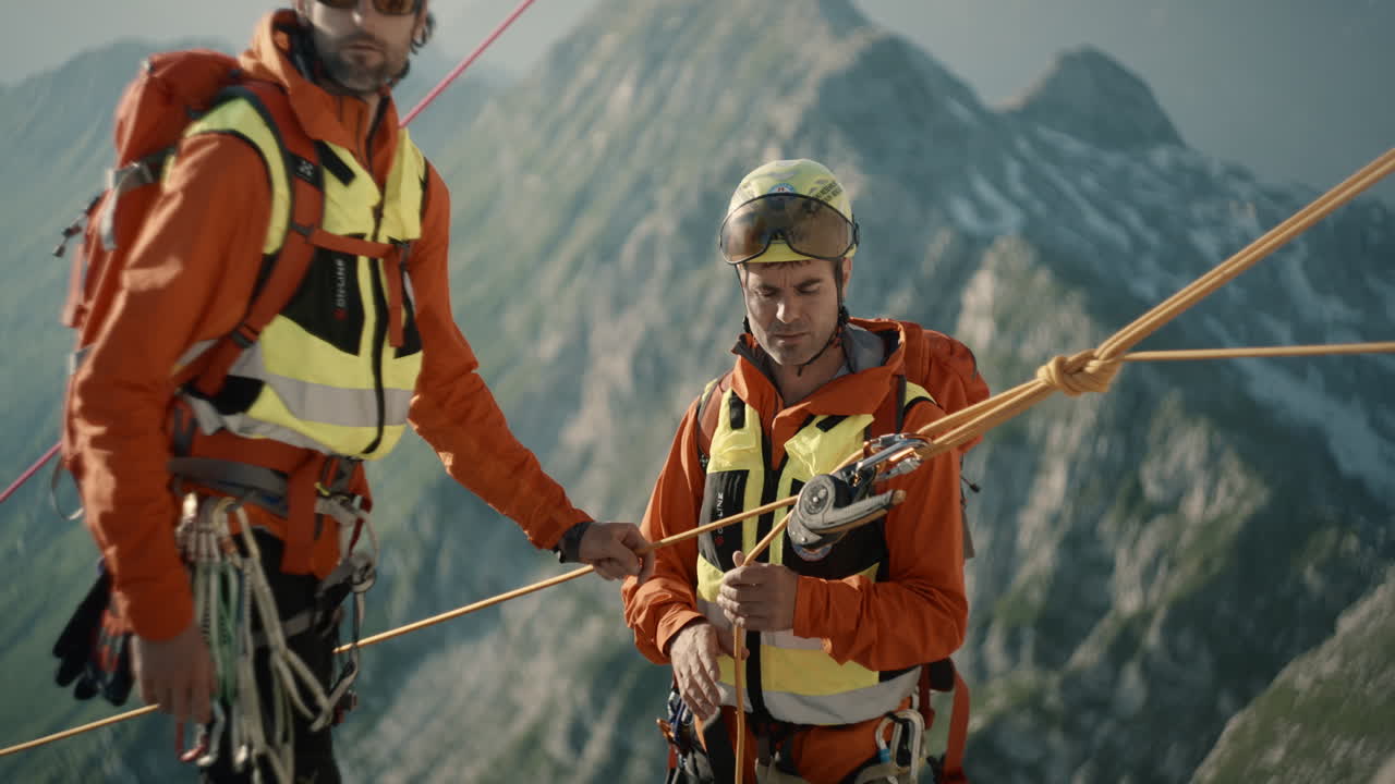 dos excursionistas en equipo de escalada naranja atando cuerdas para un descenso seguro hasta el valle