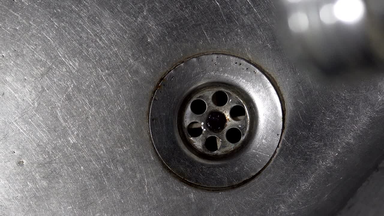 Water drops dripping from a tap into a kitchen sink, cinematic background loop