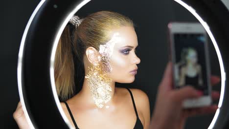 view in the mirror of a beautiful long-haired model with stylish golden makeup and covered in golden metallic pieces making