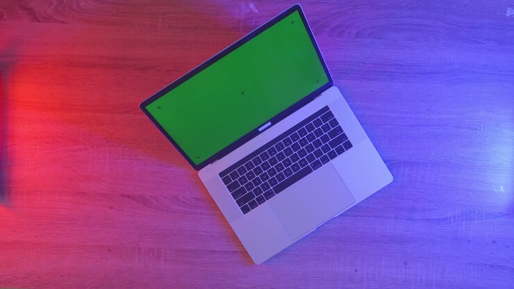 Laptop mit Greenscreen auf Holztisch mit farbigen Lichtern