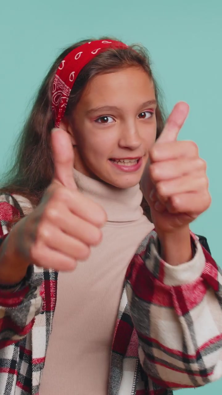 Ragazza adolescente felice ragazzino che guarda con approvazione la telecamera mostrando i pollici in alto come un segno positivo