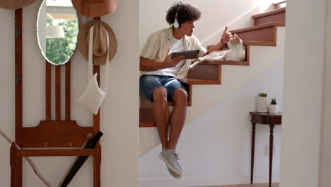 sitting on stairs, man using tablet and talking to cat in cozy home