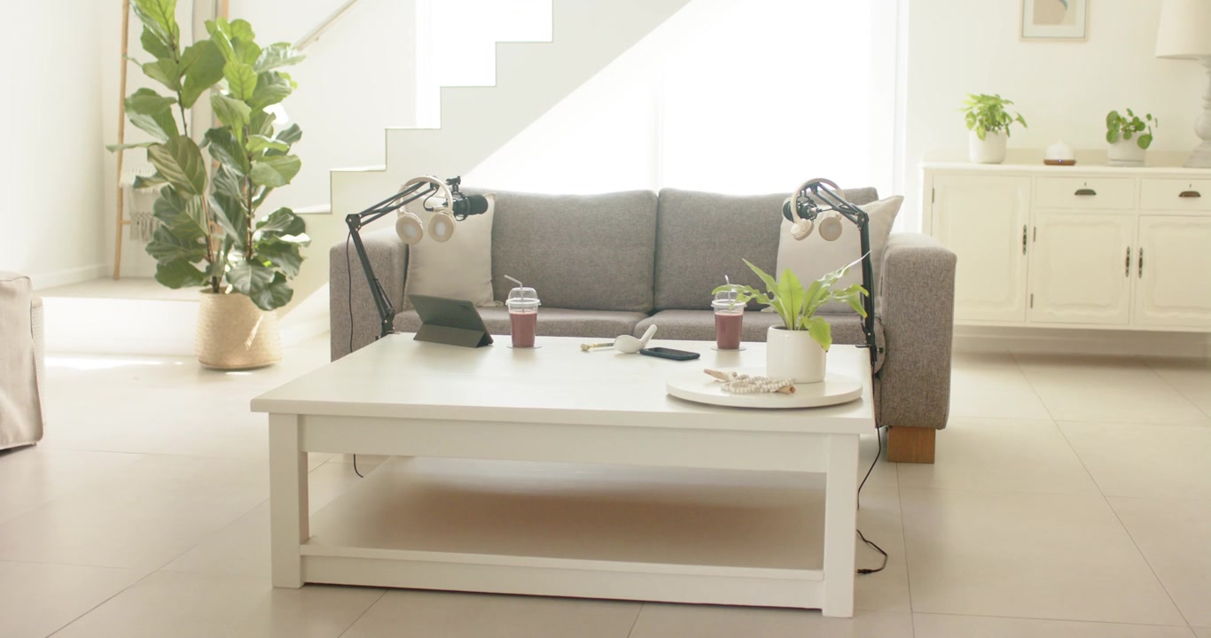 White table sitting centered, holding cups, tablet, phone, boom mics, bright window shifting light