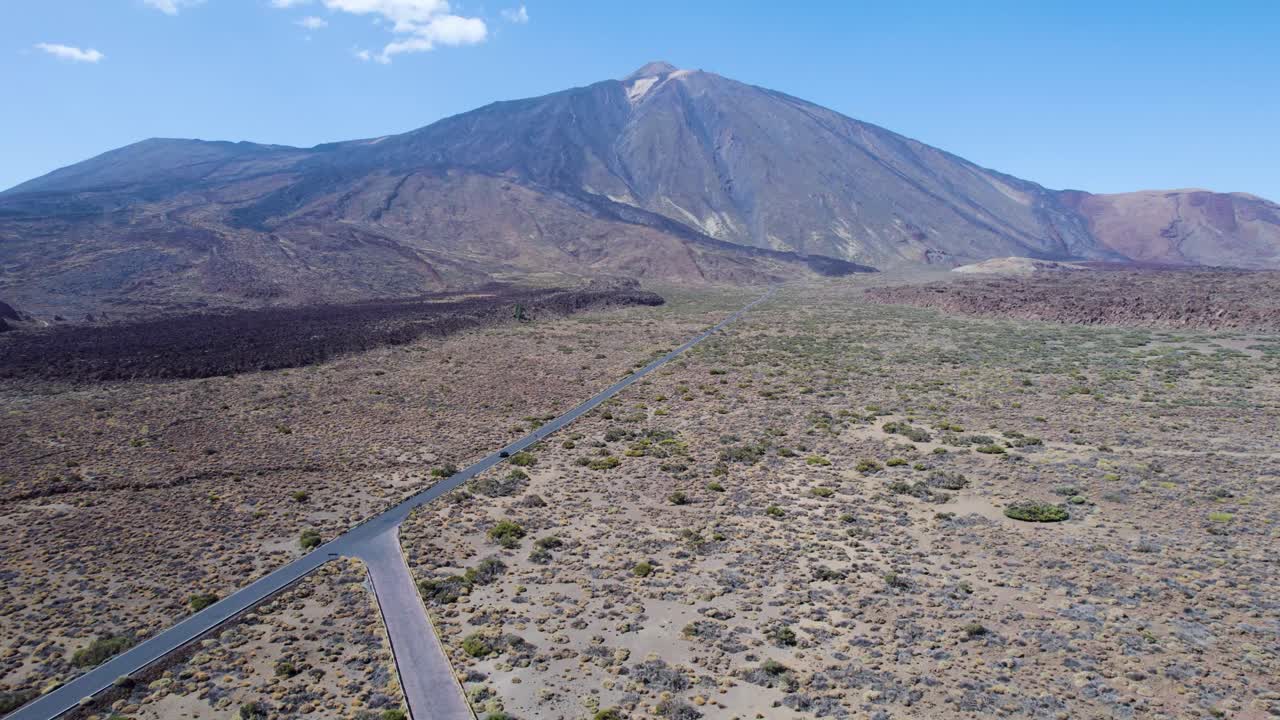 Filmato aereo di un drone che avanza verso il vulcano Teide lungo una strada rettilinea, con un'auto in lontananza che attraversa il paesaggio vulcanico di Tenerife, Spagna