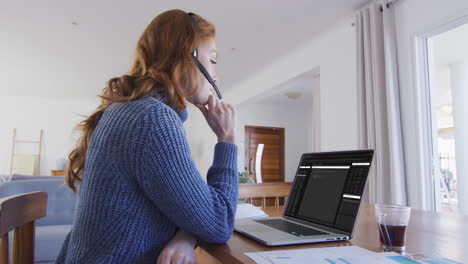 mujer caucásica sentada en un escritorio viendo el procesamiento de datos de codificación en la pantalla de una computadora portátil