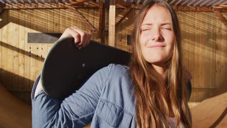 video of happy caucasian female skateboarder holding skateboard in skate park