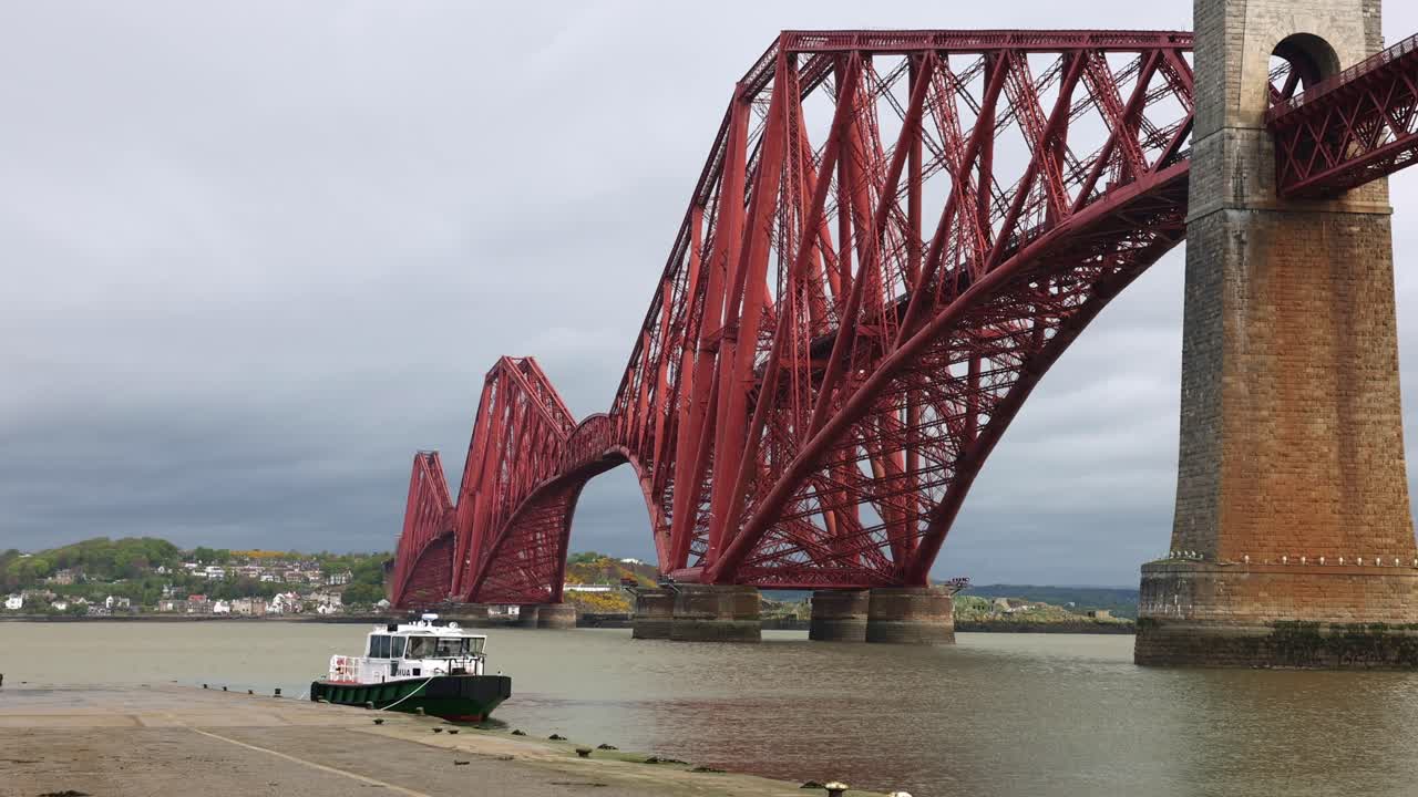 Static shot of the red Queensferry bridge with boats docked on a rainy day
