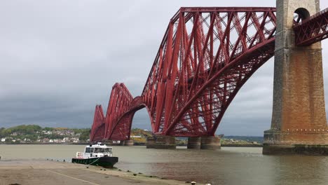 static shot of the red queensferry bridge with boats docked on a rainy day