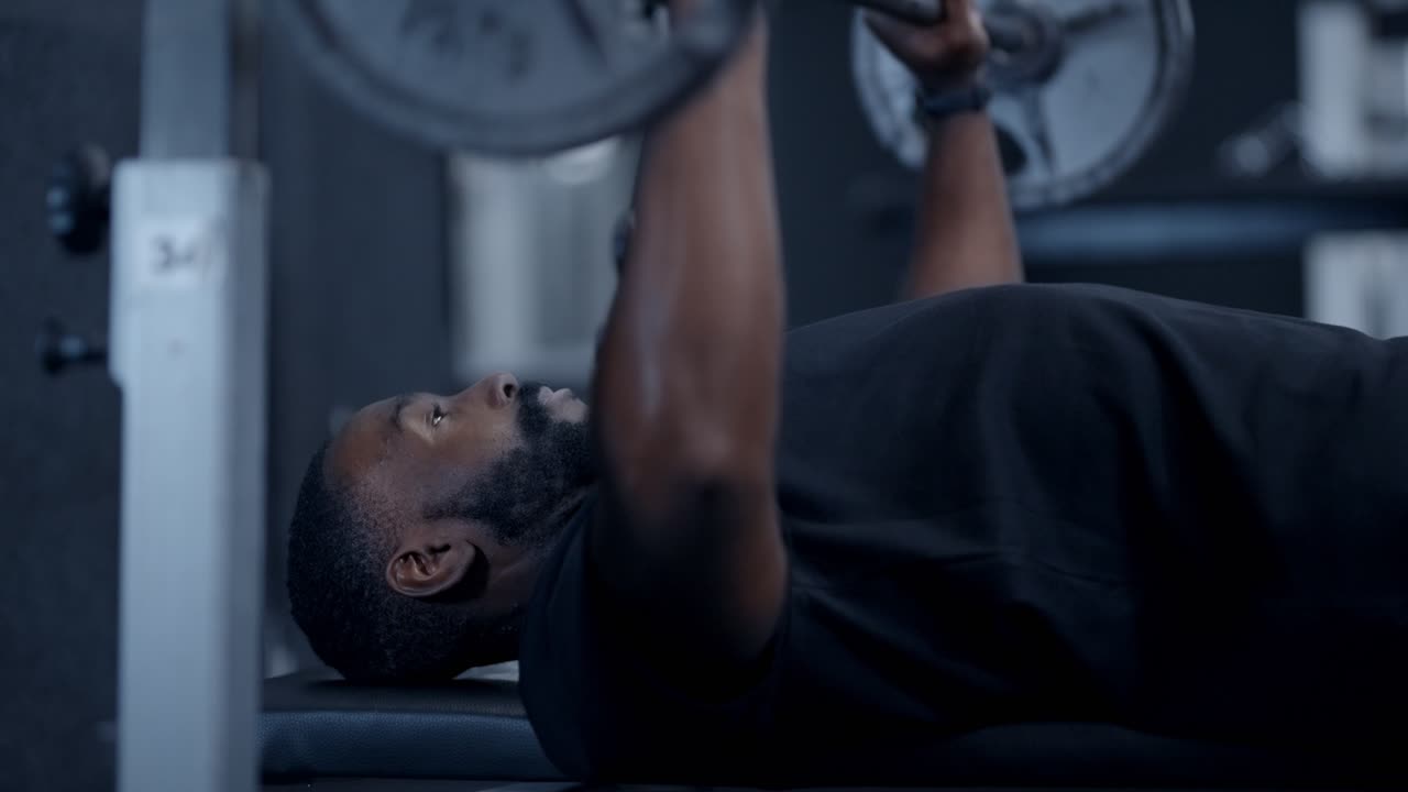 Atletik Afrikalı Amerikalı bir adam ağırlık kaldırıyor (bench press yapıyor).